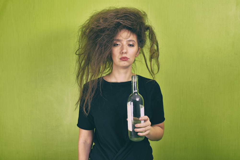 A drunk woman with messy hair while holding a bottle of wine