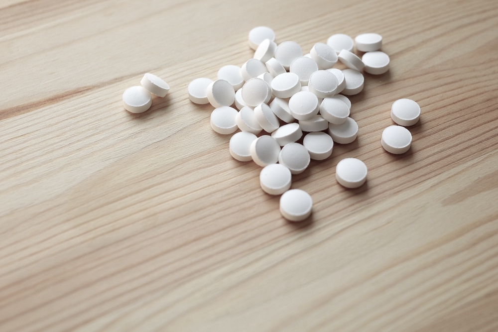 Group of Tizanidine pills lies on wooden light brown surface.