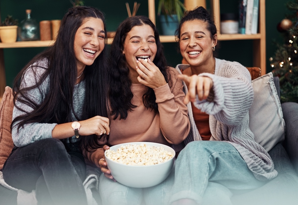 Young women having popcorn and watching tv together during New Year's Eve at home.