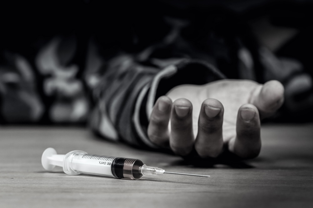 A man's hand lying on the floor beside an injectable cocaine