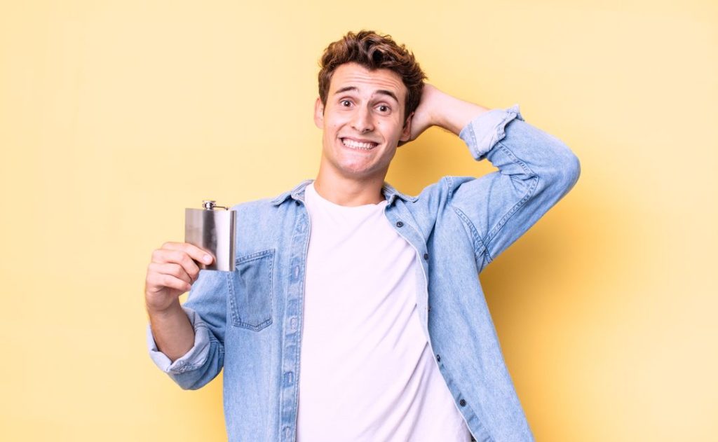 A man holding a flask that contains alcohol in a yellow background