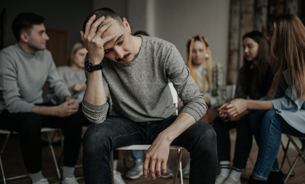 A depressed man surrounded by people with addiction problems