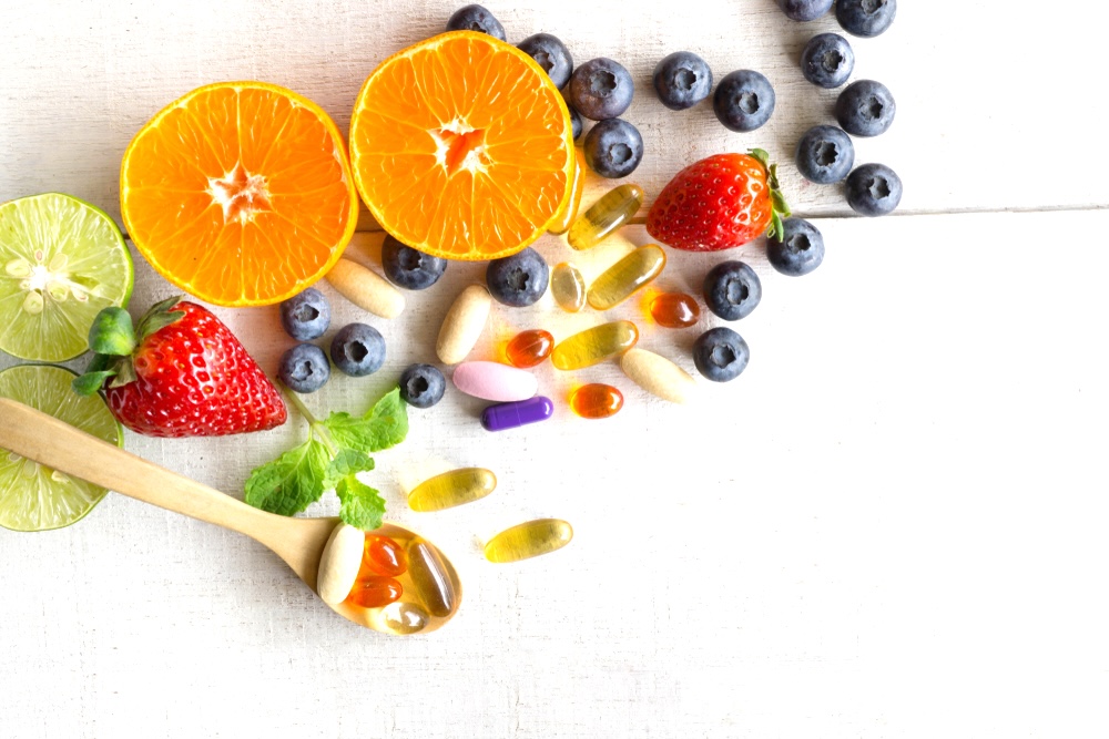 Variety of vitamin pills and fresh fruits on a table surface