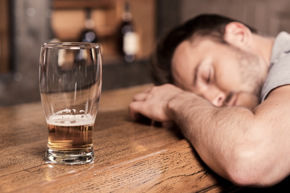 Unconscious man on a bar table with a glass of beer that’s almost empty