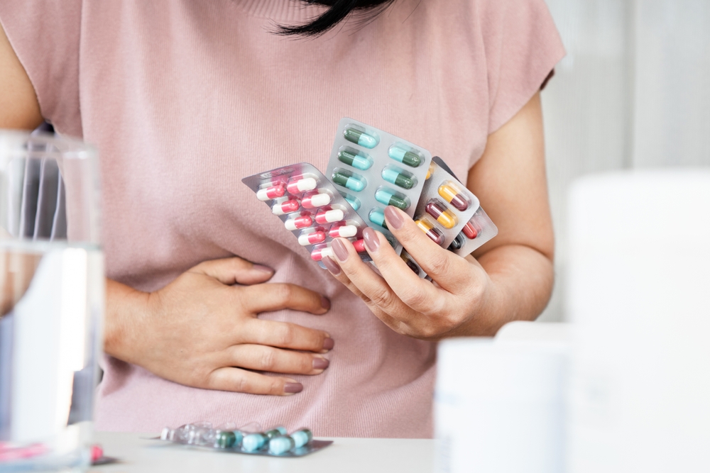 Person holding different types of pills and holding on to his stomach