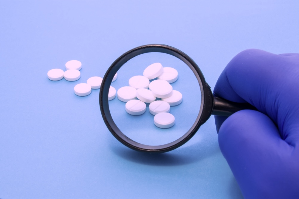 A hand with gloves using a magnifying glass over the scattered Oxycodone Pills