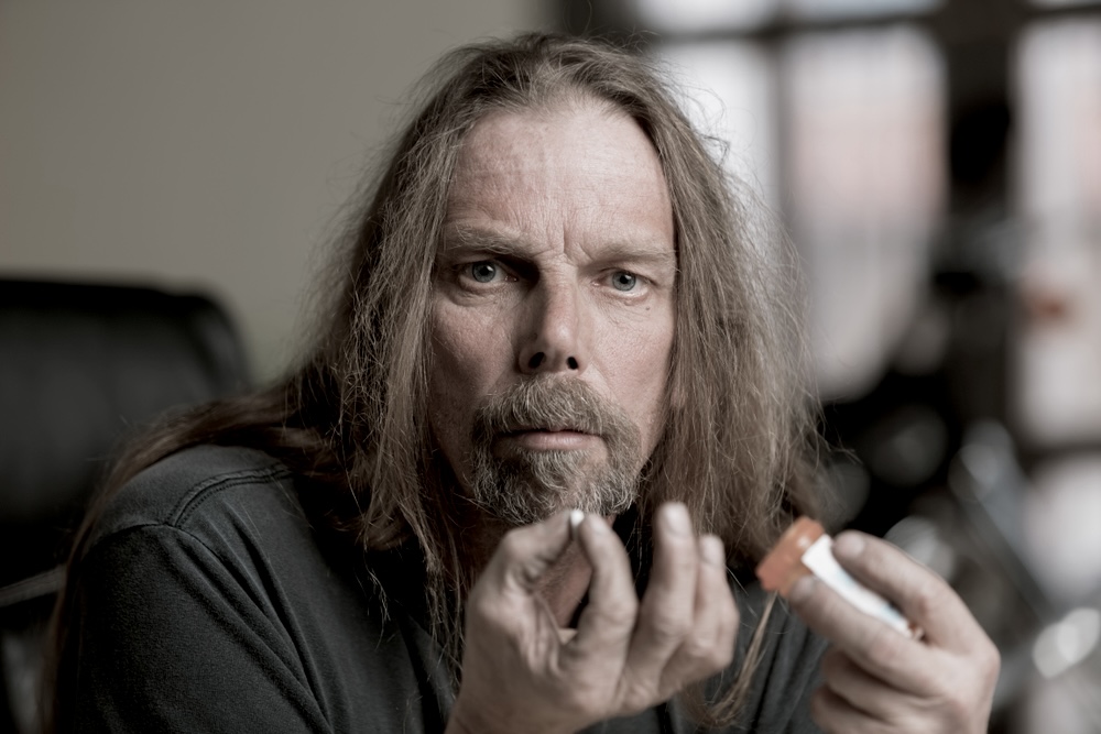 Man with long hair holding a bottle of oxycodone pills