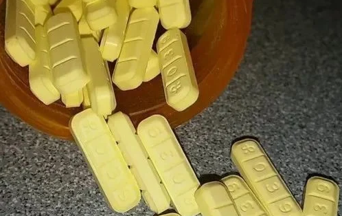 Yellow R039 pills on a gray surface from a drug container