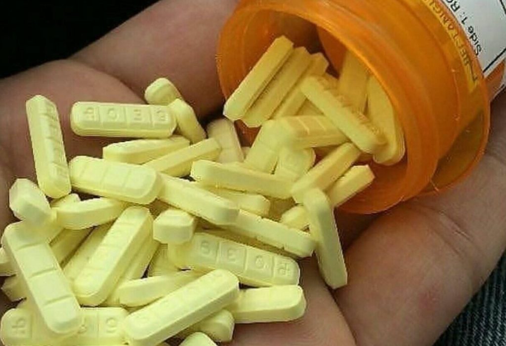 Yellow Xanax bars on the palm of a hand coming out of an orange medicine bottle