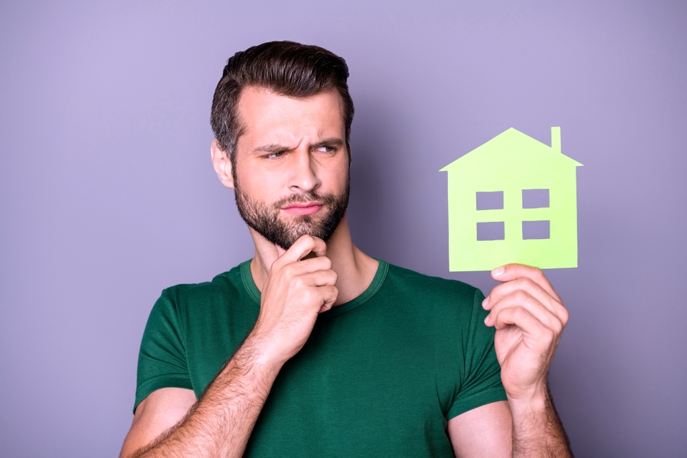 A guy with beard holding a paper card house wondering if a residential treatment is right for him