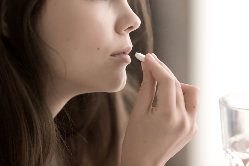 Close up image of woman putting Tizanidine in mouth.