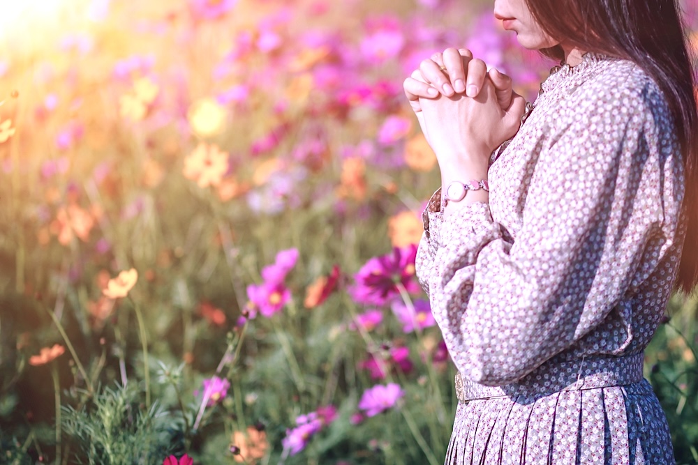 Woman praying with flowers behind her