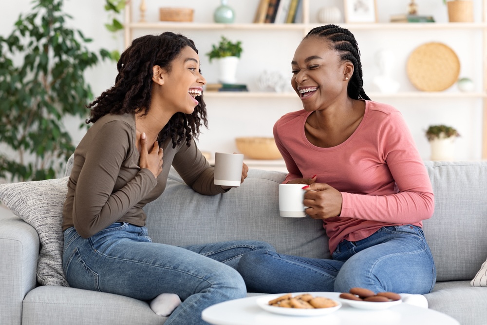 Two female friends in addiction recovery chatting and having coffee on the couch